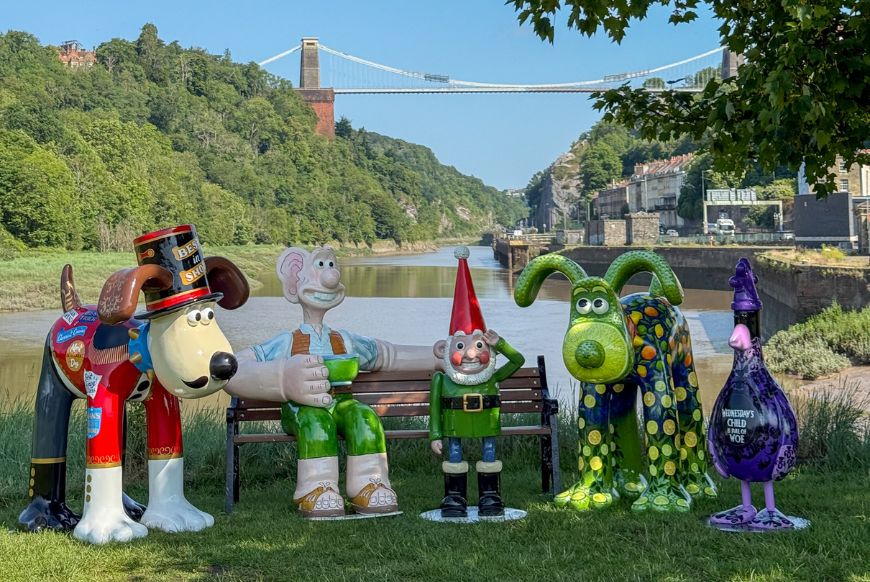 several wallace and gromit stautues photgraphed in front of the suspension bridge